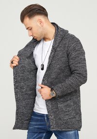 Gray knit cardigan with shawl collar, open front, two pockets, and textured pattern. Worn over a white t-shirt and paired with blue jeans.