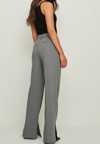 Graue weit geschnittene Hose mit seitlichen Schlitzen, aus einem glatten Stoff gefertigt. Verfügt über zwei Gesäßtaschen und eine taillierte Passform an der Taille.