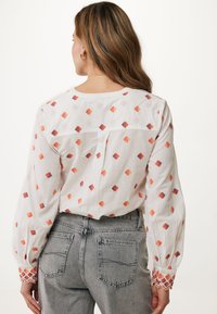Camicia bianca a maniche lunghe con motivi a rombi multicolori, dotata di polsini testurizzati e dettaglio plissettato sul retro, abbinata a jeans grigi.
