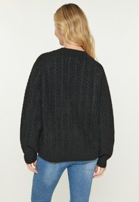 Pulover negru din tricot cu un guler rotund, umeri căzuți și mansete răsucite, realizat dintr-un material texturat și cald.