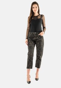 Bodysuit negro de manga larga con mangas de malla con estampado de lunares, combinado con pantalones de cintura alta con un diseño de estampado animal oscuro. Tacones negros.