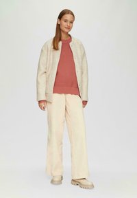 Crème gebreide jas met drukknopen, geribde rozen sweater en brede beige broek, gecombineerd met chunky beige laarzen. Soepele texturen en een losse pasvorm.