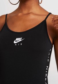 Svart Nike linne med tunna axelband, med en vit Nike-logotyp framtill och texten "AIR" på sidan i vitt. Slät tygtextur.