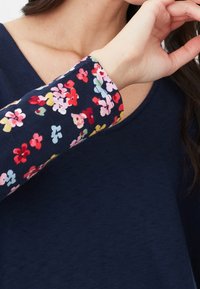 Marinblå långärmad topp med ett blommönster vid ärmsluten i röd, gul, rosa och blå. Mjuk textur med en avslappnad passform.