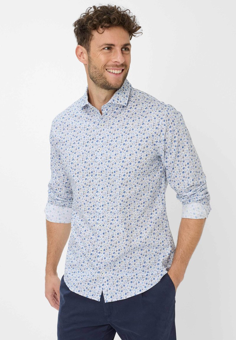 Camicia azzurra a maniche lunghe con un motivo floreale in diverse tonalità di blu. Tessuto di cotone con maniche arrotolate fino al gomito.