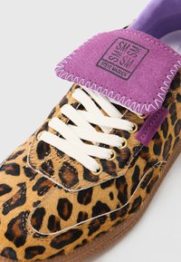 Tenisky s leopardím vzorom, s chlpovým zvieracím textúrou, bielymi šnúrkami, zlatými očkami a fialovým semišovým jazykom so šitými detailmi a značkovaním.