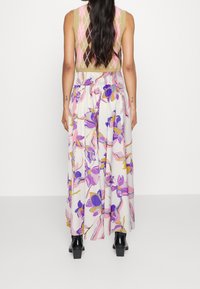 Blommig maxikjol med vit bas, som har lila och rosa blommiga mönster. Elastisk midja och en flödig design. Slät tyg och knämlängd.