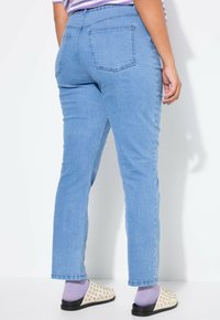 Ljusblå denimjeans visade från baksidan, med två bakfickor och rak bendesign. Kombinerade med spikade slip-on skor.