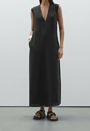 Black sleeveless maxi dress with a deep V-neck, minimalist design, and side pockets; paired with black strappy sandals.