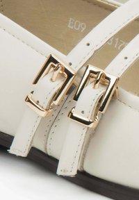 Białe skórzanebuty z dwoma złotymi klamrami i cienkimi paskami. Gładka faktura z przeszyciami i zaokrąglony czubek.