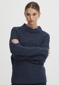 Pull en maille bleu marine avec un col haut, présentant un motif texturé et un ourlet côtelé, fabriqué à partir d'un tissu doux et confortable.
