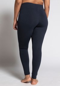 Tmavomodré legíny z pružného materiálu, s vysokým pásom, priliehajúcim strihom a zúženými nohavicami; hladká textura s minimálnymi švami.