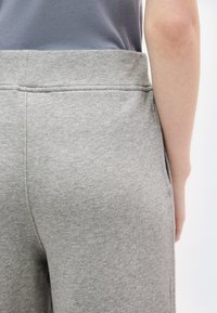 Κοντινό πλάνο ενός ατόμου που φορά ανοιχτό γκρι φόρμα και σκούρο γκρι πουκάμισο μπαλωμένο μέσα, εμφανίζοντας λεπτομέρειες στην πίσω και πλαϊνή ραφή.