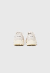 Lacoste sneakers in light beige with a textured mesh upper, featuring a cushioned sole and branded tabs on the heels.