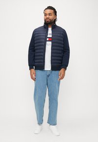 Laivastonsininen untuvatakki, jossa on vaakasuorat tikkauskohdat ja korkea kaulus, yhdistettynä valkoiseen t-paitaan ja vaaleansinisiiin suoralahkeisiin farkkuihin. Valkoiset lenkkarit.