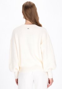 Maglione oversize color crema realizzato in materiale a maglia testurizzata con spalle scese e orlo a coste. Piccola etichetta del marchio sul retro.