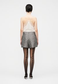 Camisola de seda con detalles de encaje, shorts de tweed gris y medias negras con patrones de corazones, combinados con tacones de punta.