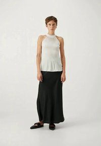 Witte geribbelde haltertop gecombineerd met een vloeiende zwarte maxi-jurk en zwarte platte schoenen. De look heeft zachte texturen en een getailleerd silhouet.