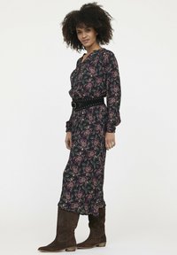 Langes Blumenkleid in Dunkelblau mit creme- und burgunderfarbenen Blumenmustern, ausgestattet mit langen Ärmeln, einem gebundenen Ausschnitt und einem breiten schwarzen Taillengürtel.