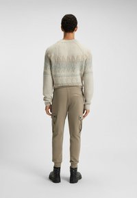 Strickpullover mit einem hellbeigen Grundton und blauen Akzenten; Cargo-Hosen in Khaki mit seitlichen Taschen, kombiniert mit schwarzen Stiefeln.