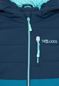 Tamsiai mėlynas pamušalu džemperis su turkio spalvos vidumi, su centriniais užtrauktukais, šoninėmis kišenėmis ir "TROLLKIDS" logotipu ant krūtinės.