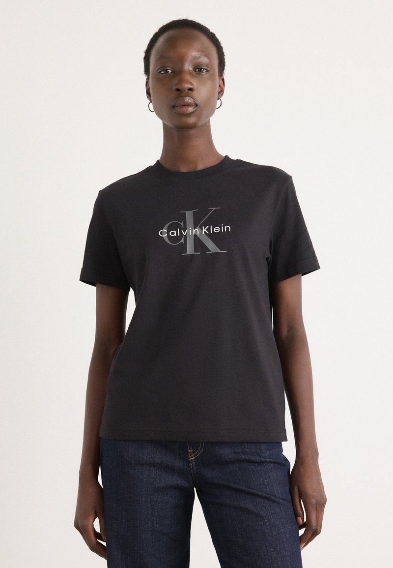 T-shirt en coton noir avec un graphic frontal de "Calvin Klein" et un grand "K" en imprimé argenté. Manches courtes et col rond.