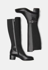 Bottes noires montantes en cuir lisse, avec des panneaux latéraux élastiques et une fermeture éclair sur le côté. Elles disposent d'un talon carré et d'un accent de boucle.