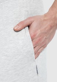 Hellgraue, strukturierte Shorts aus Baumwollmischung mit Seitentaschen; Hand ruht in der Tasche. Kleines Etikett an der Seitennaht sichtbar.