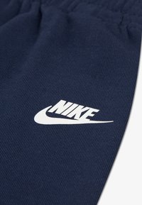 Αθλητικό παντελόνι σε ναυτικό μπλε από υφασμά υφής, με λευκό λογότυπο Nike. Η ελαστική μέση προσφέρει ρυθμιζόμενη εφαρμογή.