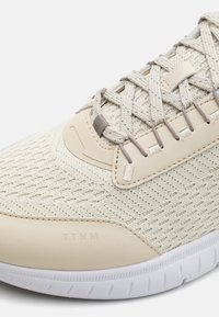 Beige mesh joggesko med teksturert stoffsokkel, plastdetaljer og tonede snøringer. Hvit gummisåle med mønster. Merkevarelogo preget.