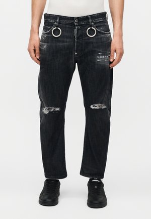 Sorte slidte jeans med revnede knæ og sølv ringe fastgjort til forreste bæltestropper, båret med sorte sneakers og en hvid top.