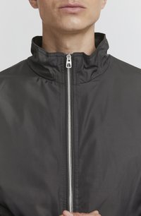 Black zip-up jacket with a high collar, featuring a silver zipper and a smooth, lightweight texture. Simple design, no visible patterns.