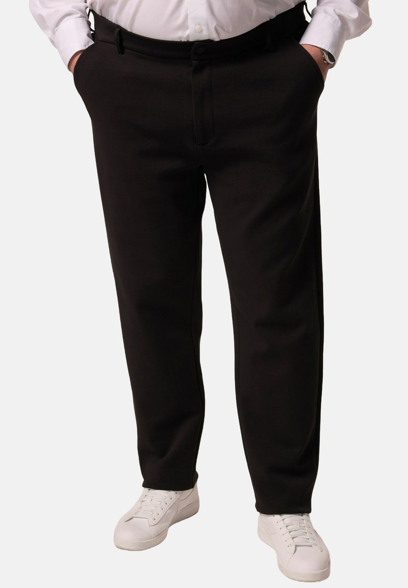 Pantalones negros con una textura suave, diseño ajustado, bolsillos laterales y cierre de botón frontal, combinados con zapatillas blancas.