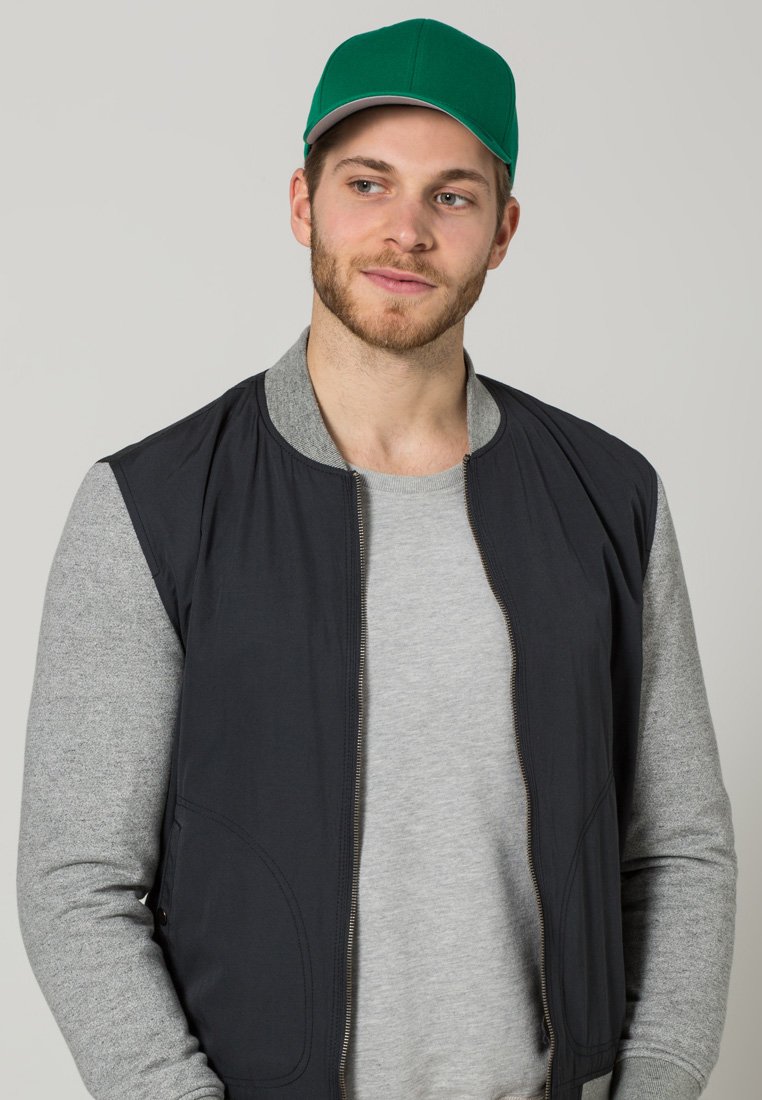 Chaqueta bomber negra con cremallera y mangas grises, llevada sobre una camiseta gris, complementada con una gorra verde con visera gris contrastante.
