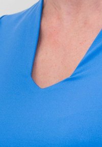 Top de corte en V en tela azul sólido. Textura suave con un brillo moderado. Presenta mangas cortas y un diseño ajustado.