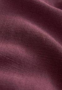 Tissu bordeaux avec une surface lisse, légèrement texturée ; aspect léger et légèrement scintillant. Aucune motif ou accent distinct visible.