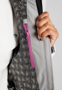 Grå jacka med svart-vitt prickigt foder. En rosa dragkedjeficka är framträdande, med en texturerad känsla och slät yta.