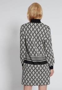 Abito a fantasia bianco e nero con colletto alto a coste, maniche lunghe e vita aderente, presenta forme geometriche e un tessuto texturizzato.