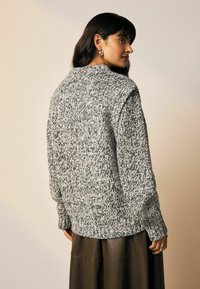 Grober Strickpullover in Grau und Schwarz, mit einem lockeren Schnitt, weiten Ärmeln und einem strukturierten Muster. Kombiniert mit einem braunen Lederrock.