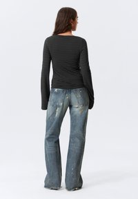 Μακρυμάνικη μαύρη και γκρι ριγέ μπλούζα σε συνδυασμό με ξεθωριασμένο μπλε τζιν παντελόνι με φθαρμένες λεπτομέρειες και ξεφτισμένα τελειώματα.