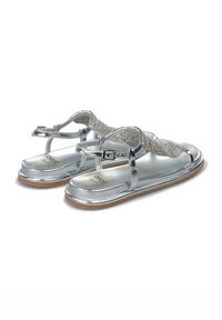 Srebrne sandały z teksturowanym paskiem, metalicznym wykończeniem, regulowanym zapięciem i płaską podeszwą z delikatnym brązowym akcentem na spodzie.