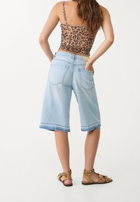 Culottes de mezclilla azul claro con dobladillo deshilachado, dos bolsillos traseros y una cinturilla marrón. Combinados con una camiseta sin mangas de estampado de leopardo y sandalias.