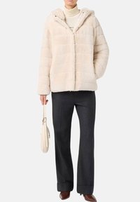 Faux fur jas in lichtbeige met een capuchon, voorzien van gestructureerde strepen, knopen aan de voorkant en zijzakken, gecombineerd met zwarte broeken en een lichte tas.