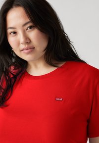 T-shirt rossa in cotone con scollatura a girocollo. Presenta un piccolo etichetta Levi's bianca e rossa sul petto. Tessuto liscio, vestibilità casual.