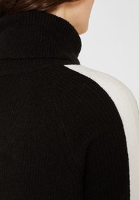 Czarnobiały teksturowany dziany sweter z wysokim golfem, widoczny z tyłu i z boku, noszony przez osobę z brązowymi włosami.