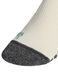 Bijela čarapa s teksturiranim gornjim dijelom i tamnosivim prstom. Ima zeleni logo sa strane, kontrastne boje i rebrasti materijal za bolje prianjanje.