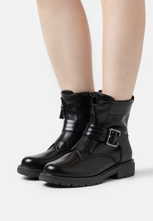 Black leather ankle boots with a shiny finish, featuring a zip closure, strap accent, and buckle detail. Low, textured rubber sole.