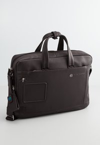Borsa per laptop in pelle marrone scuro con due manici superiori, tracolla staccabile, tasca con zip frontale e finitura texturizzata.