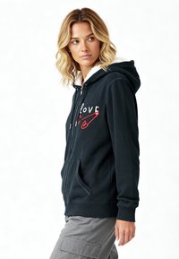 Hoodie zippé bleu marine avec doublure en fourrure, présentant un graphique "love" rouge et blanc, une poche kangourou et des poignets côtelés.