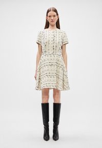 Sūnu piedurkņu A formas kleita krēmkrāsā ar melniem vertikāliem svītrainiem. Tekstila audums ar piestiprinātu jostasvietu un izplūdušu svārku. Saskaņota ar melniem augstiem zābakiem.